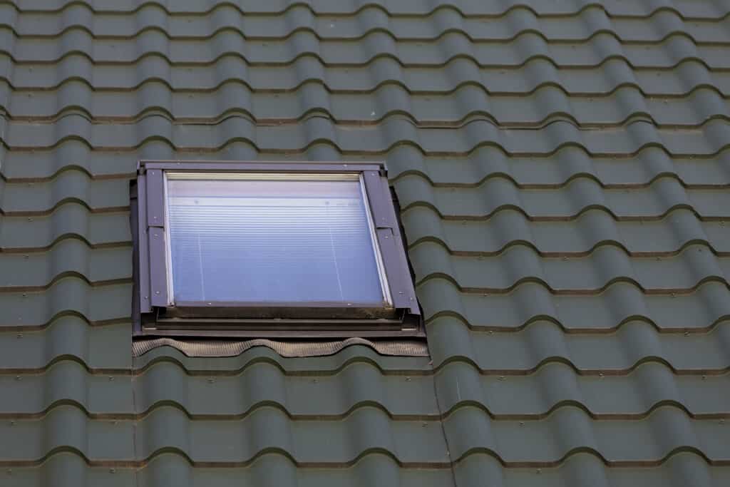 Une petite fenêtre Velux sur un toit de tuiles vertes.