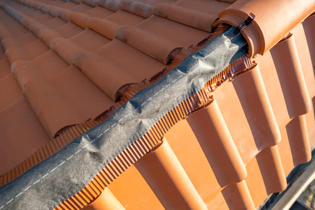 Un toit de tuiles avec un tuyau métallique fixé à son faitage.
